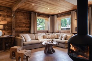 A cozy cabin interior with a wooden ceiling, a sofa with cushions, a table with a vase, and a fireplace.