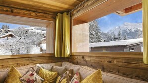 Un acogedor interior de cabaña con techo de madera, un sofá con cojines estampados y vistas a montañas nevadas.