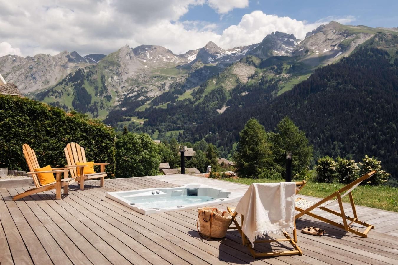 A wooden deck with a hot tub, lounge chairs, and a view of mountains.