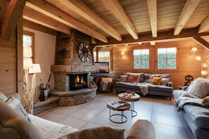 A cozy log cabin interior with a stone fireplace, wooden beams, and a comfortable seating area.