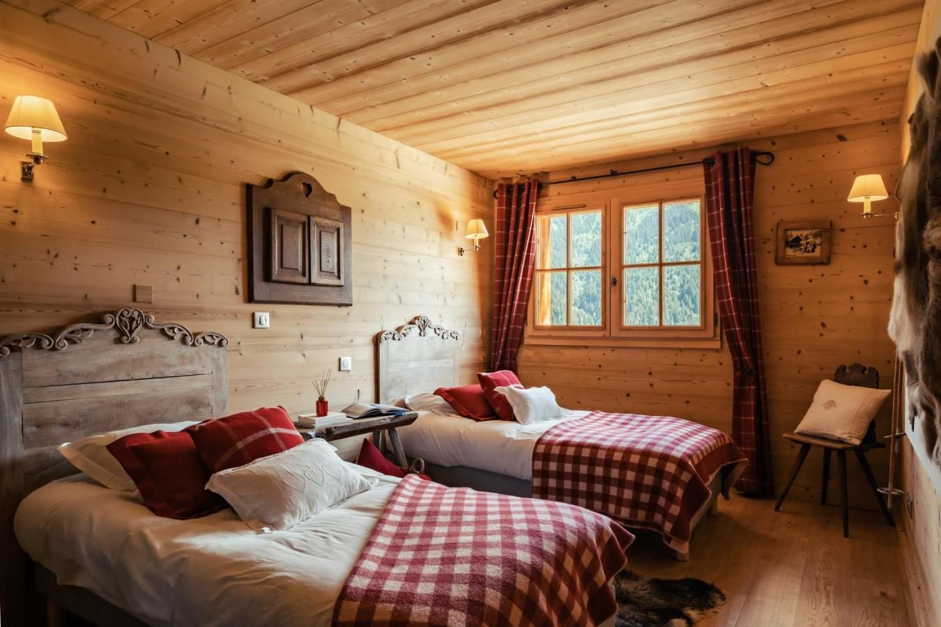 A cozy room with two beds, wooden walls, and a window with curtains.