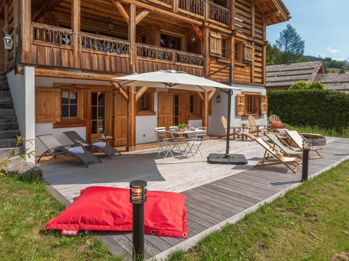 Un chalet en bois doté d’une terrasse, d’un espace salon extérieur et d’un coussin rouge.