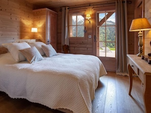 Ein gemütliches Schlafzimmer in einer Holzhütte mit einem großen Bett, zwei Nachttischlampen und Blick ins Freie durch eine Tür.