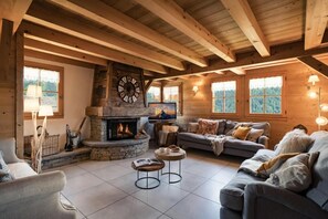 Ein gemütliches Wohnzimmer mit Kamin aus Stein, Holzbalken, einer Couch und einem Fernseher.