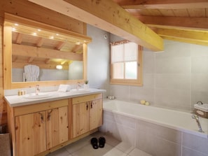 Ein Badezimmer im Holz-Blockhausstil mit einem Doppelwaschbecken, einem großen Spiegel, einem Fenster und einer Badewanne.