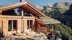 A wooden cabin with large windows, a deck, and a mountain view.