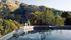 A hot tub with a mountain view, two glasses, and a bottle on a tray.