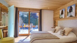 A bedroom with a large bed, a desk, and a chair. There is a sliding glass door leading to an outdoor area.