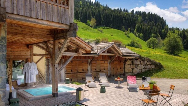 A wooden cabin with a hot tub, lounge chairs, and a stone wall.