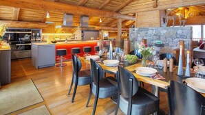 A spacious kitchen with wooden beams, a stone wall, and a dining area with a table set for six.