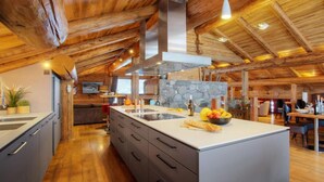 A spacious kitchen with a large island, wooden ceiling beams, and a stone accent wall.