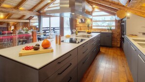 A modern kitchen with a large island, wooden ceiling beams, and a view of the outdoors.