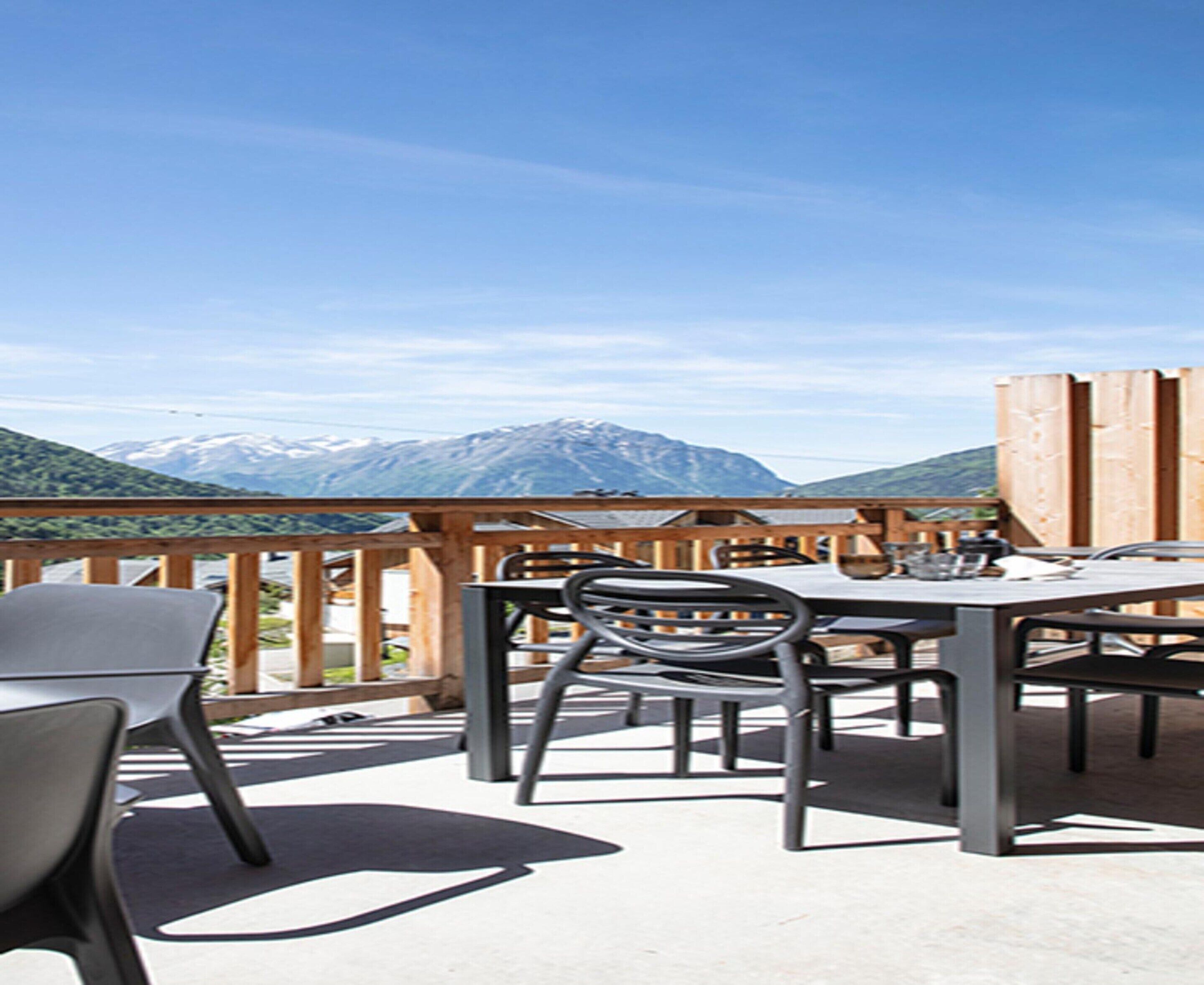 An outdoor patio with a table and chairs, overlooking a mountainous landscape.