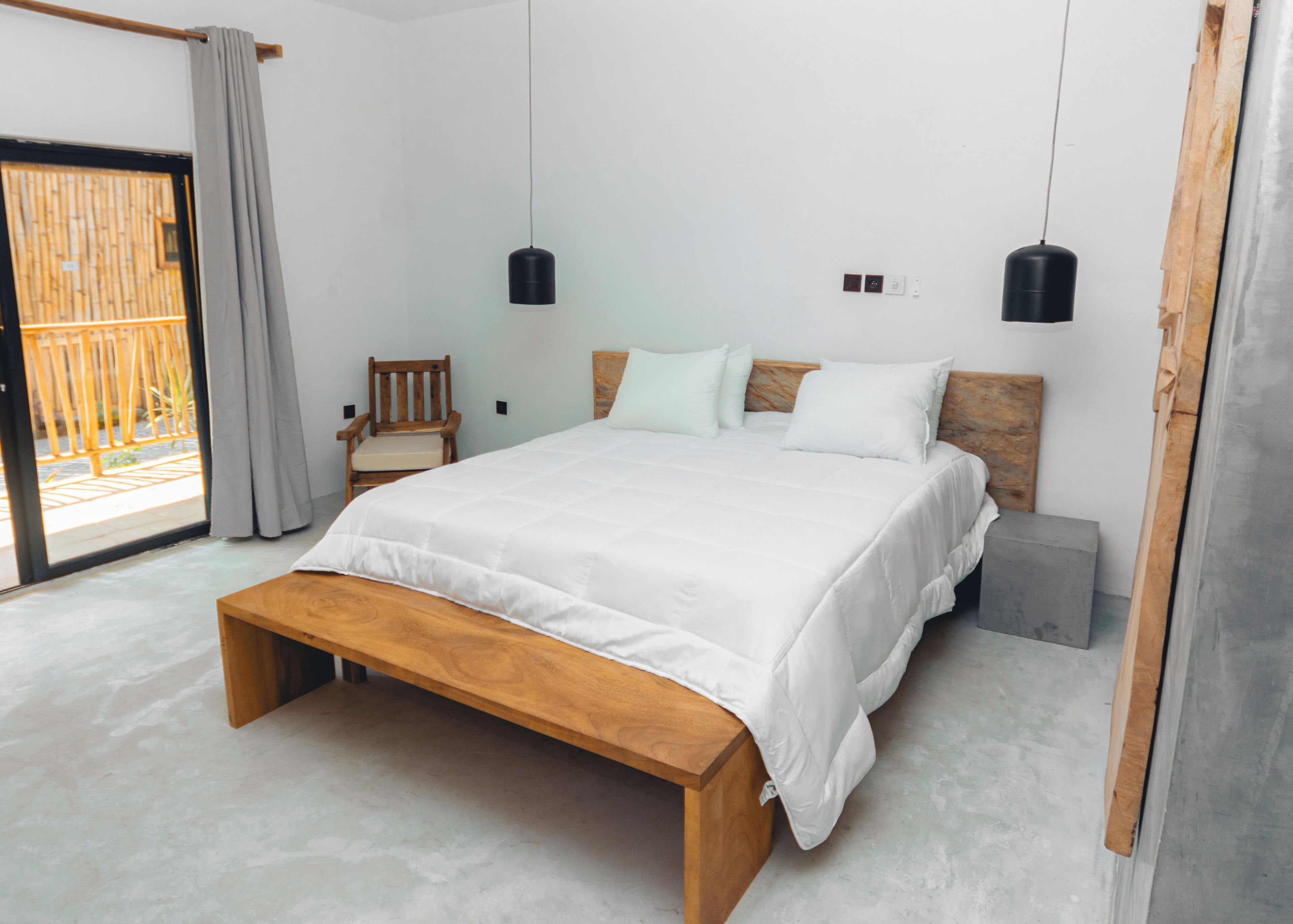 A bedroom with a wooden bed, a bench, a chair, and two hanging pendant lights.
