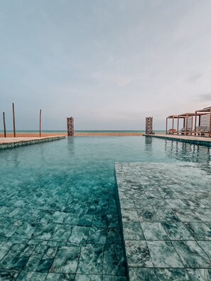 A clear pool with a tiled deck, a beach view, and a wooden structure with lounge chairs. - MIADJOE BEACH RESORT (Aného)