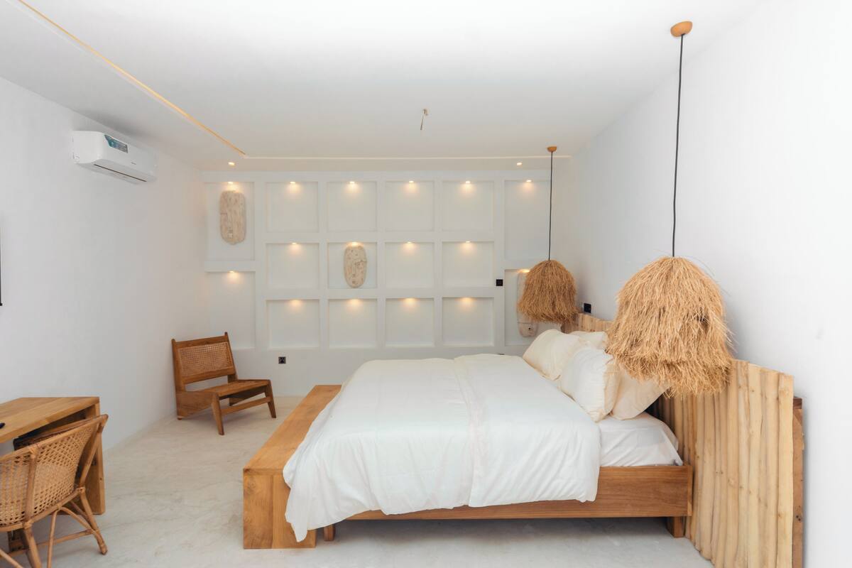 A minimalist bedroom with a wooden bed, a desk, and wicker chairs.