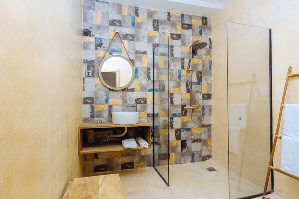 A bathroom with a tiled wall, a round mirror, a sink, and a shower. - MIADJOE BEACH RESORT (Aného)