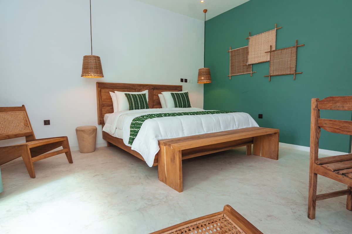 A bedroom with a wooden bed, two hanging lamps, a bench, and a woven wall hanging.