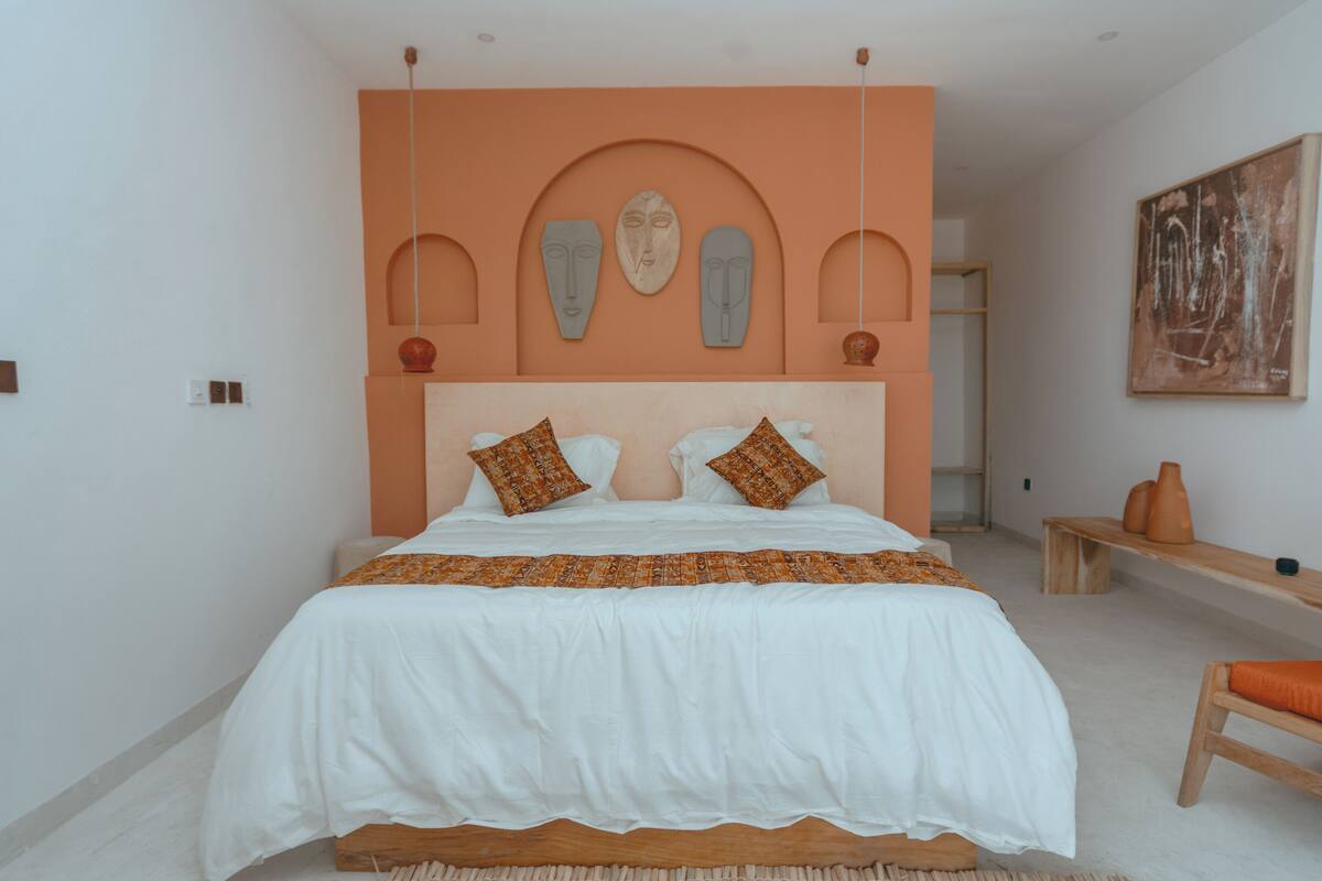 A bedroom with a large bed, a wooden bench, and a wall-mounted shelf.