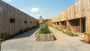 Une cour bordée de murs en bambou, avec un chemin pavé, des plantes en pot et un jardin central où se trouve un palmier.