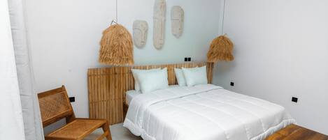 Un dormitorio con cama, un banco de madera, una silla de mimbre y un cabecero fijado a la pared.