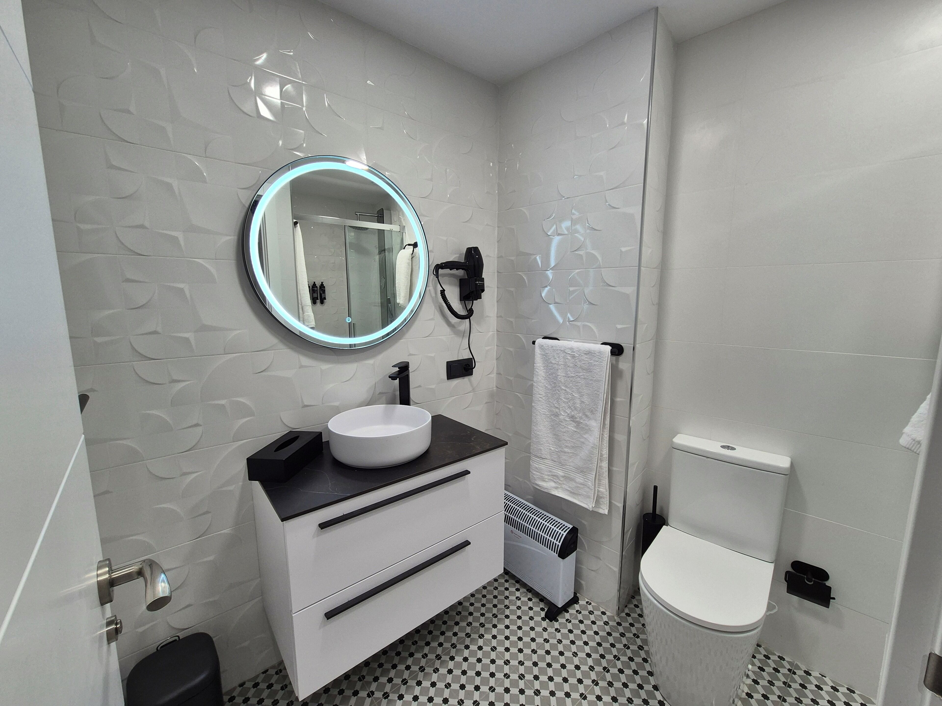 A modern bathroom with a round mirror, white sink, and black countertop.