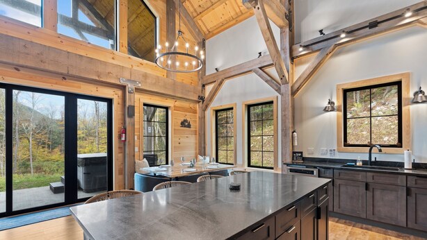 A spacious kitchen with a large island, wooden beams, and large windows offering views of the outdoors.