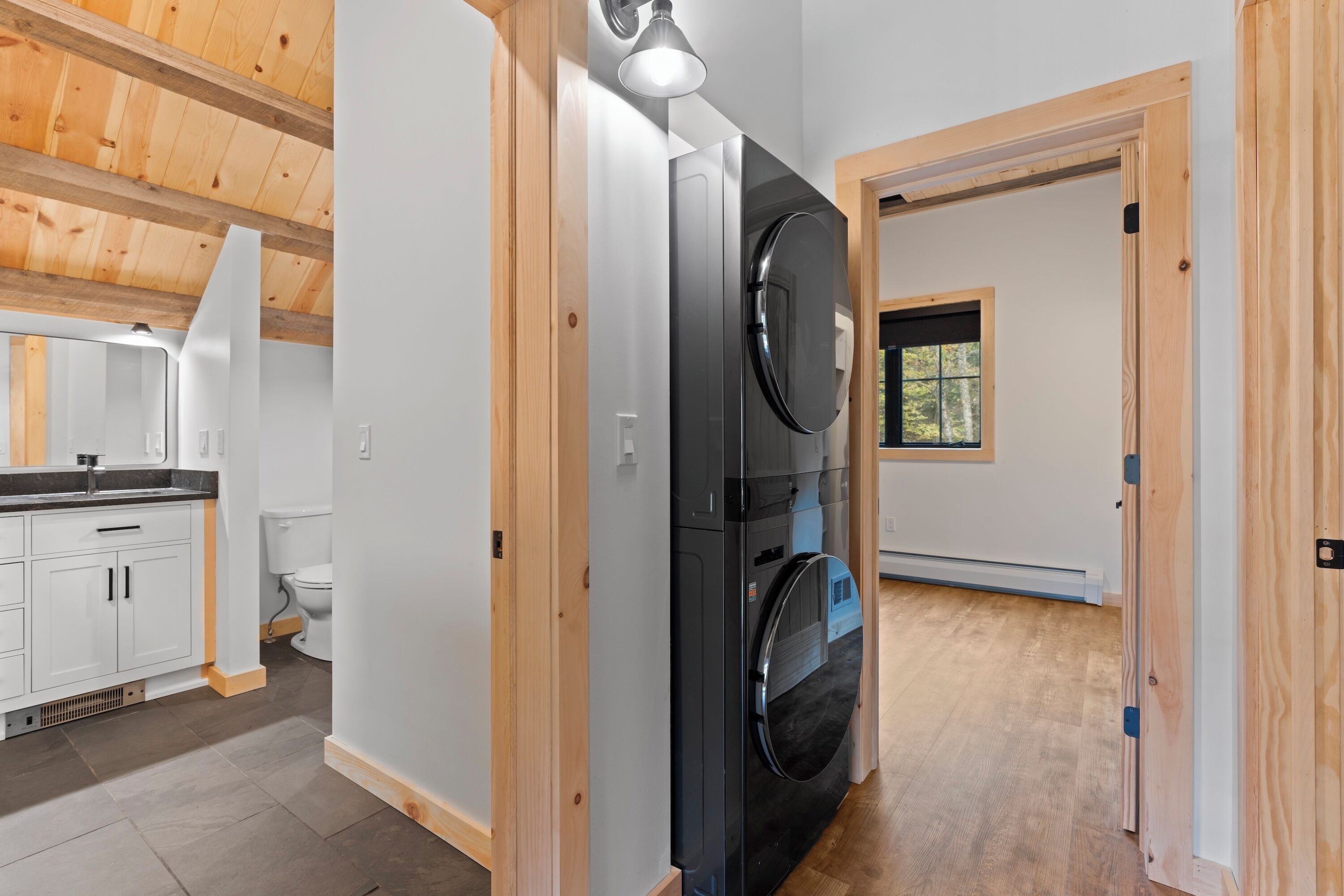 Une buanderie équipée d’un lave-linge et d’un sèche-linge, avec un plancher en bois et une petite fenêtre.