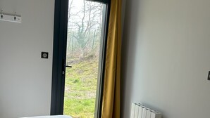 A hotel room with a bed, two rolled towels, a window with a view of the outdoors, and a radiator.