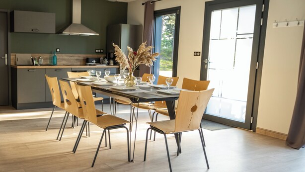 A modern dining area with a long table, chairs, and a vase of dried plants.