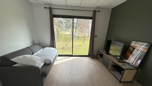 A modern living room with a sofa, a flat-screen TV, and a sliding glass door leading to a garden.