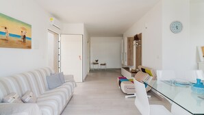 A modern living room with a sofa, a glass dining table, and a kitchen area in the background. - Appartamento Terre del Sud by BarbarHouse (Mancaversa)