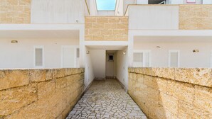 A narrow stone-paved corridor between two buildings with white walls and shutters. - Appartamento Terre del Sud by BarbarHouse (Mancaversa)