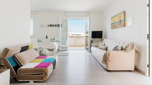 A modern living room with a sofa, a coffee table, and a TV. There is a balcony with a glass door leading outside. - Appartamento Terre del Sud by BarbarHouse (Mancaversa)
