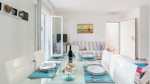 A dining area with a glass table, white chairs, and striped placemats. There is a painting on the wall and a door leading to another room. - Appartamento Terre del Sud by BarbarHouse (Mancaversa)