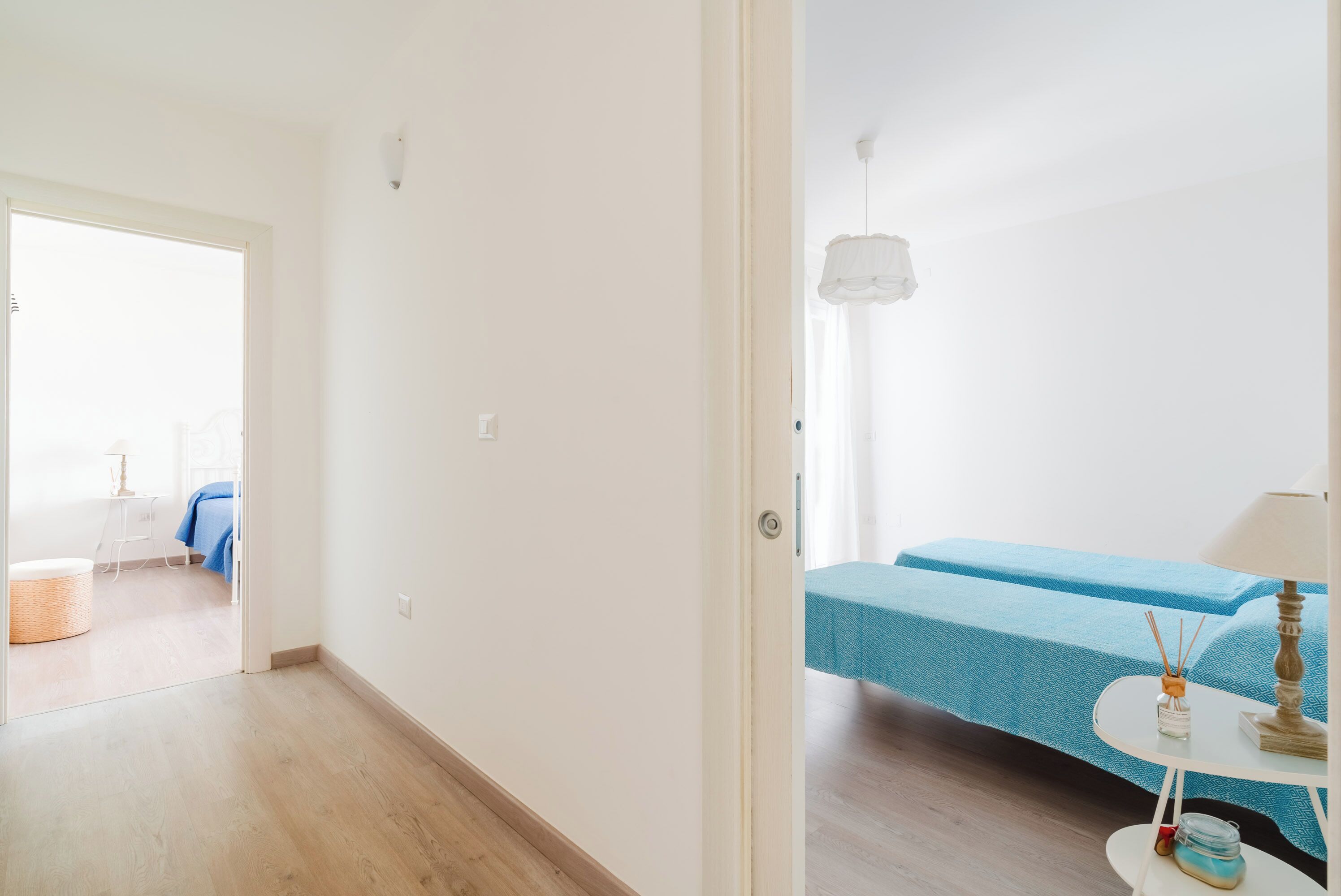 Een kamer met twee bedden, een klein tafeltje met een lamp en een rieten stoel.