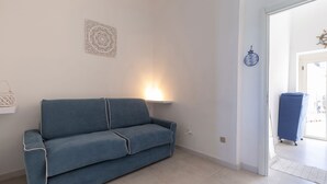 A room with a blue sofa, a wall-mounted lamp, a decorative wall piece, and a door leading to another room. - Il Faro by BarbarHouse (Vieste)