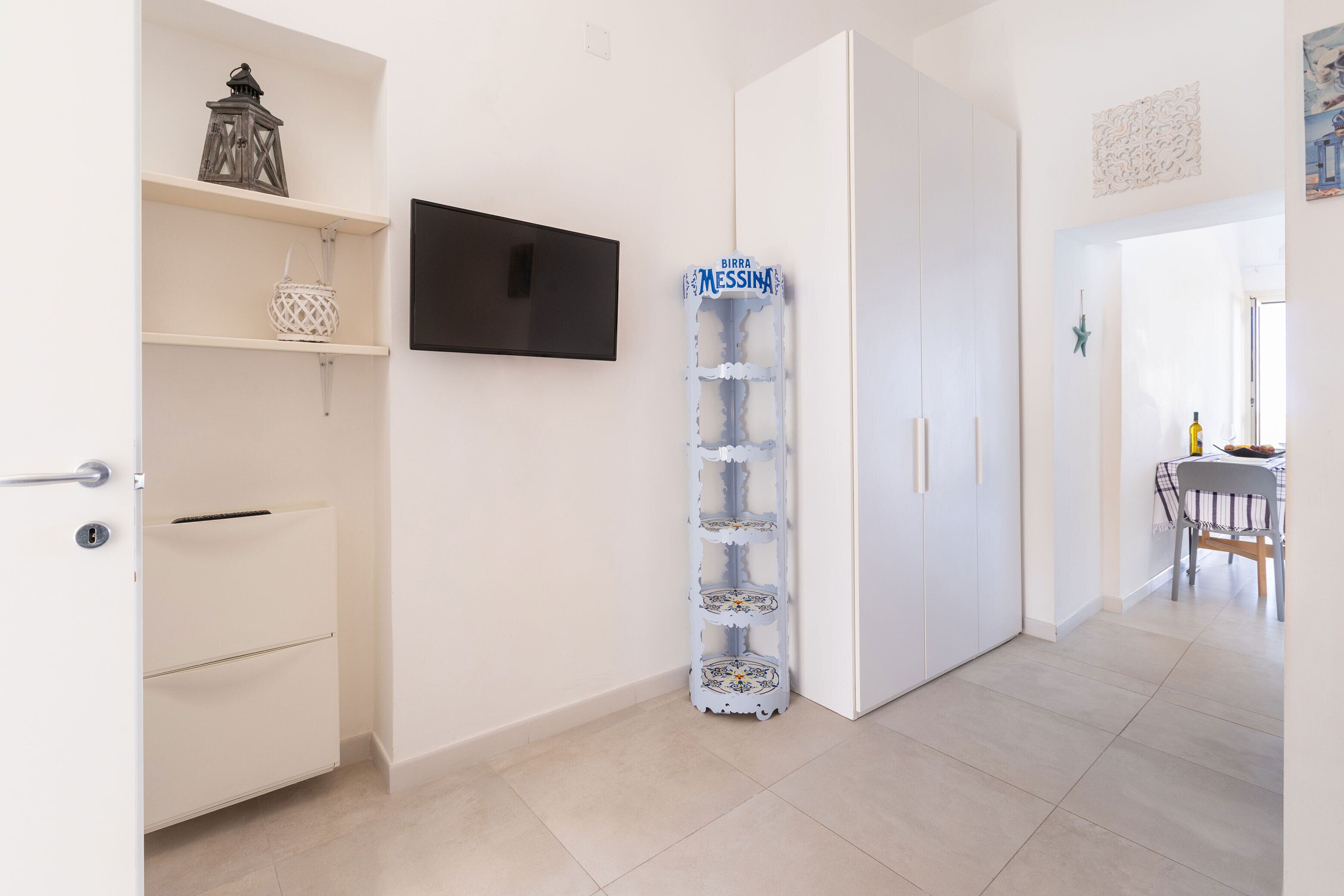 A modern kitchen with white cabinetry, a mounted flat-screen TV, and a decorative water dispenser.