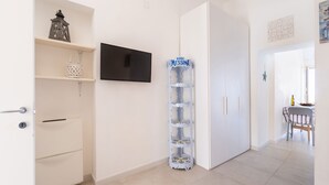 A modern kitchen with white cabinetry, a mounted flat-screen TV, and a decorative water dispenser. - Il Faro by BarbarHouse (Vieste)