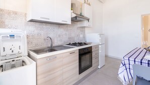 A compact kitchen with a gas stove, sink, and a built-in oven. There is a small refrigerator and a microwave on the countertop. - Il Faro by BarbarHouse (Vieste)