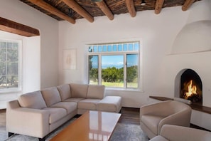 Una sala de estar con sofá modular, chimenea y ventanas amplias con vistas a la vegetación.