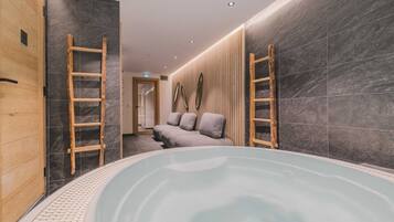 A spa room with a hot tub, wooden ladder, and a sofa with cushions.