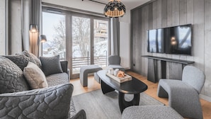 A modern living room with a large TV, grey furniture, and a view of a snowy landscape. - Apartment in Plan Peisey Near Paradiski (Peisey-Nancroix)