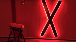 Una habitación iluminada en rojo con un cartel grande en forma de 'X' en la pared y un banco.