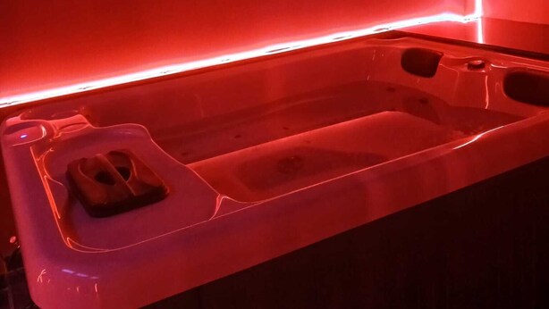 Zona de spa con iluminación roja, bañera de hidromasaje y un pequeño espacio de estar.