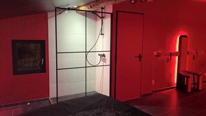 Una habitación con cama, zona de ducha y pared iluminada en rojo.