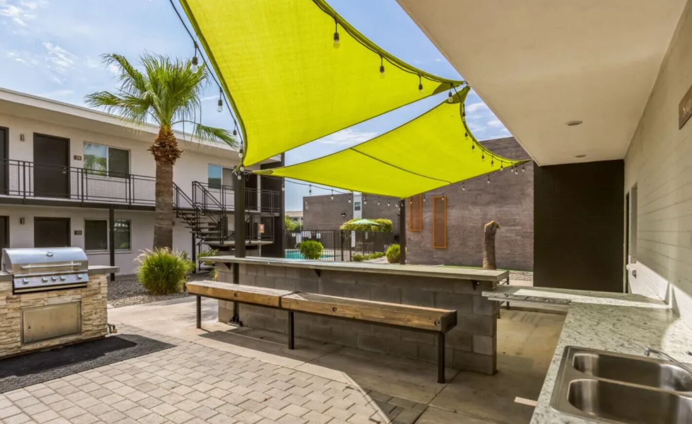 Un área de cocina al aire libre con una parrilla, un banco y ambiente junto a la piscina.