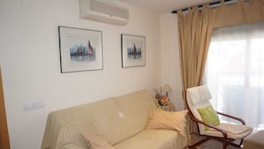 A living room with a beige sofa, a wooden armchair, two framed paintings, a lamp, and a window with curtains. - noo............................. (Sant Antoni de Calonge)
