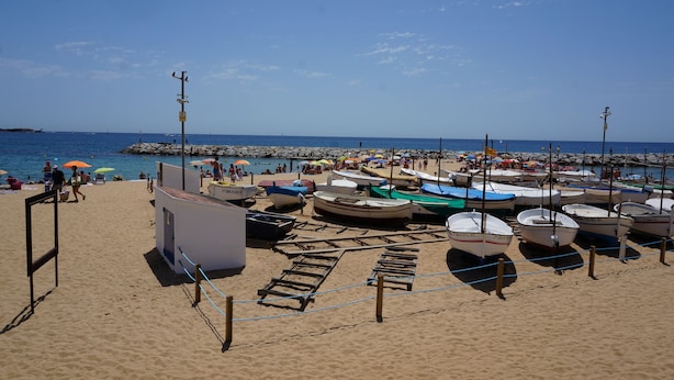 A beach with boats docked, a lifeguard tower, and a rocky breakwater. - noo............................. (Sant Antoni de Calonge)