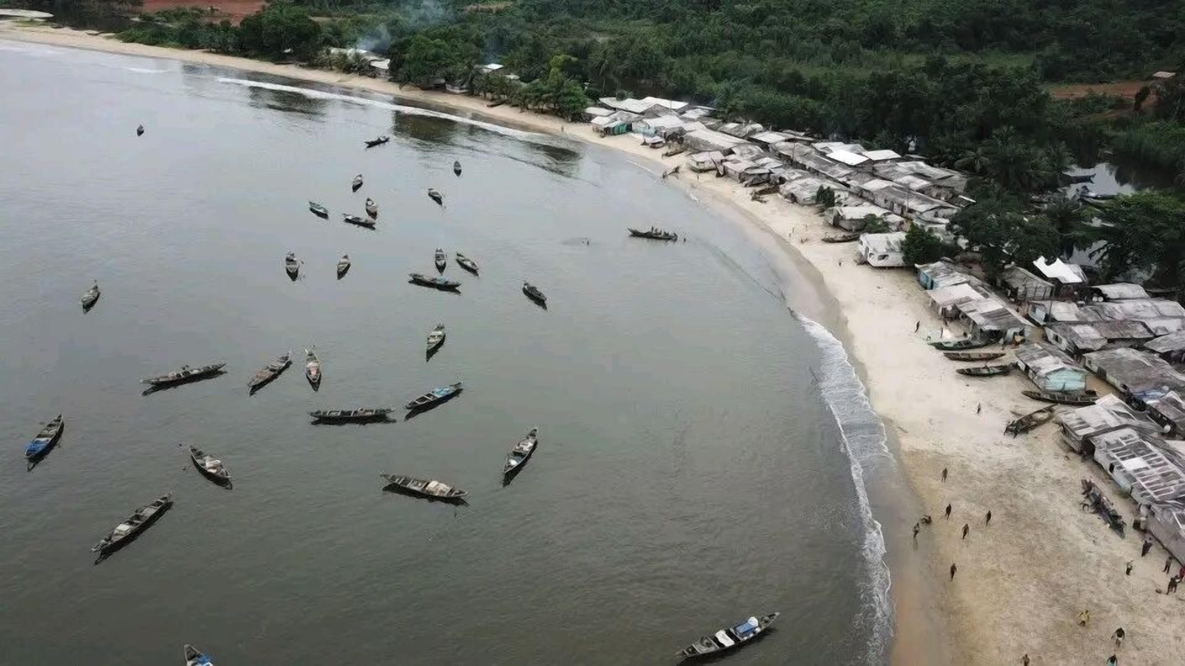 A beach with numerous boats and a row of huts along the shore.